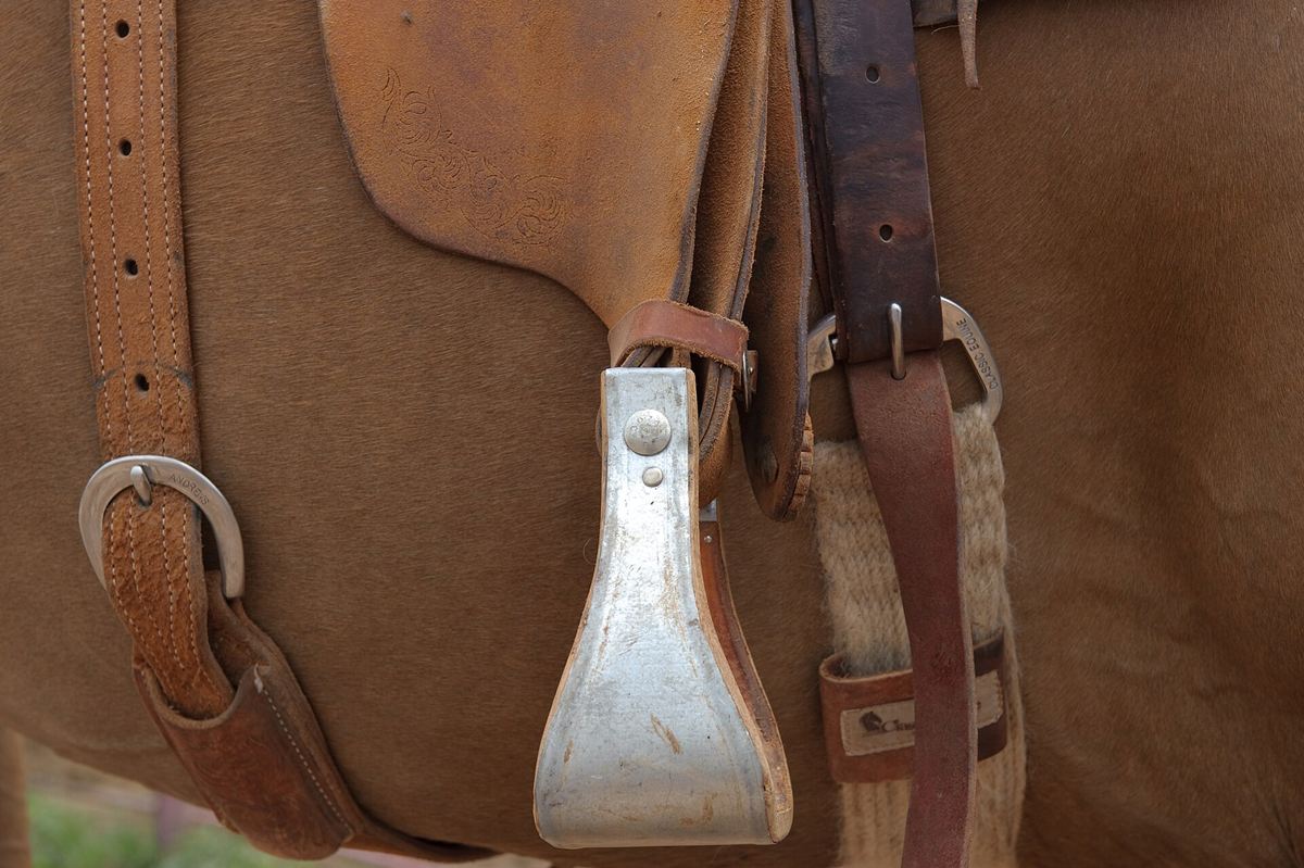 Detalle de una silla de montar de cuero marrón con estribo metálico